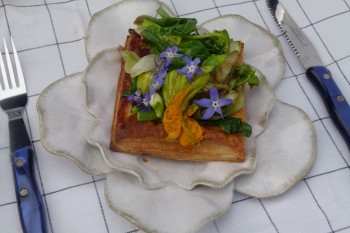 Spring vegetable and flower savory tart with goat cheese on plate