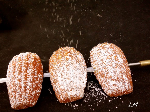 dusting powdered sugar  on three Madeleine's 