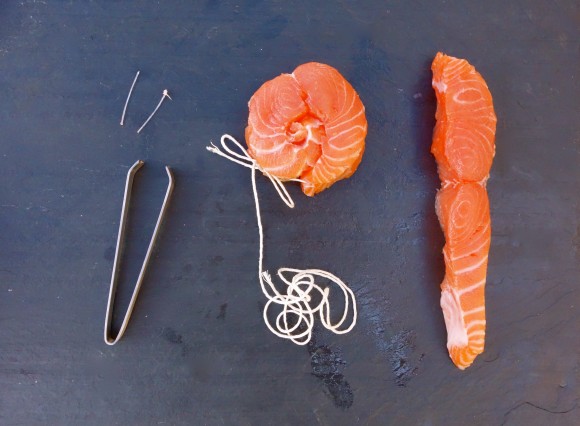 salmon filets with string and tongs one filet has been rolled and tied with string